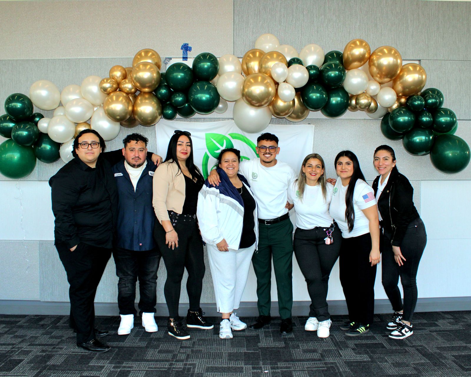 A group photo under green, white and gold balloons