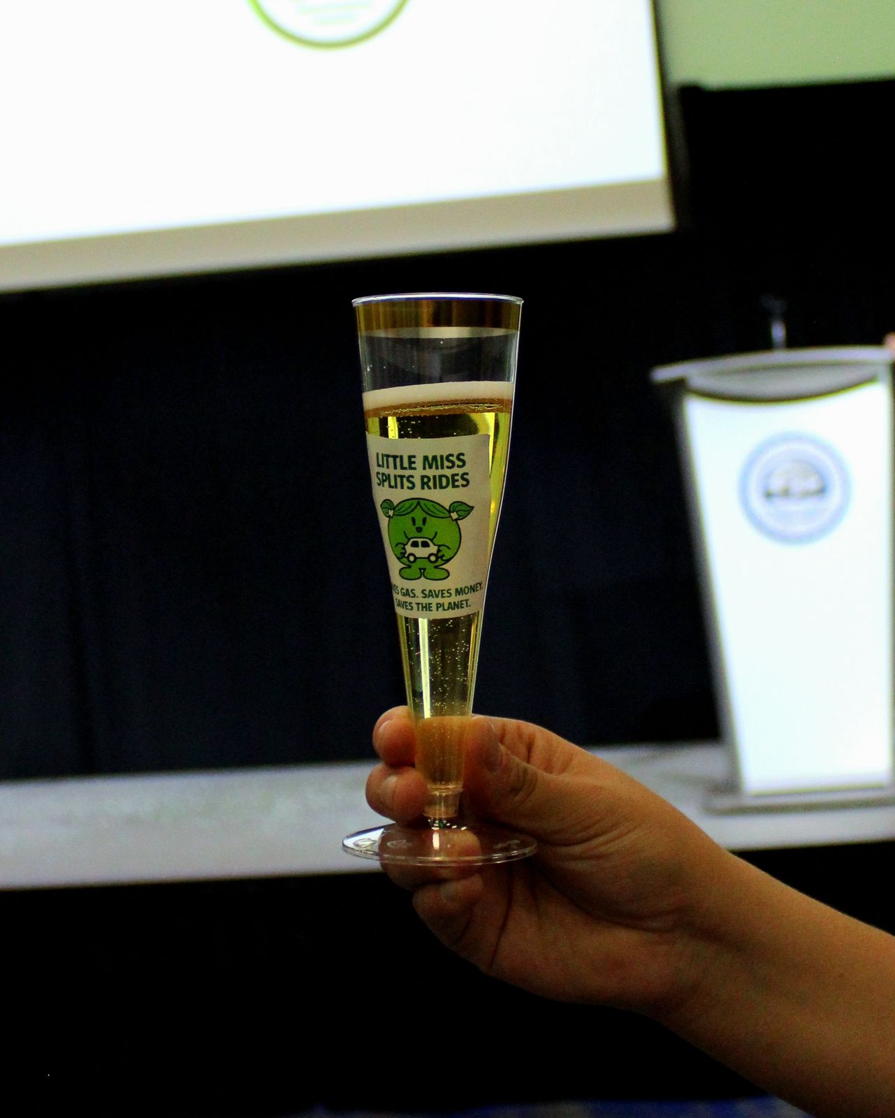 A hand raising a Ride Splits-branded glass toward the stage